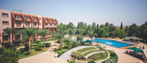 A hotel with a swimming pool, landscaped gardens, and a multi-story building with balconies.