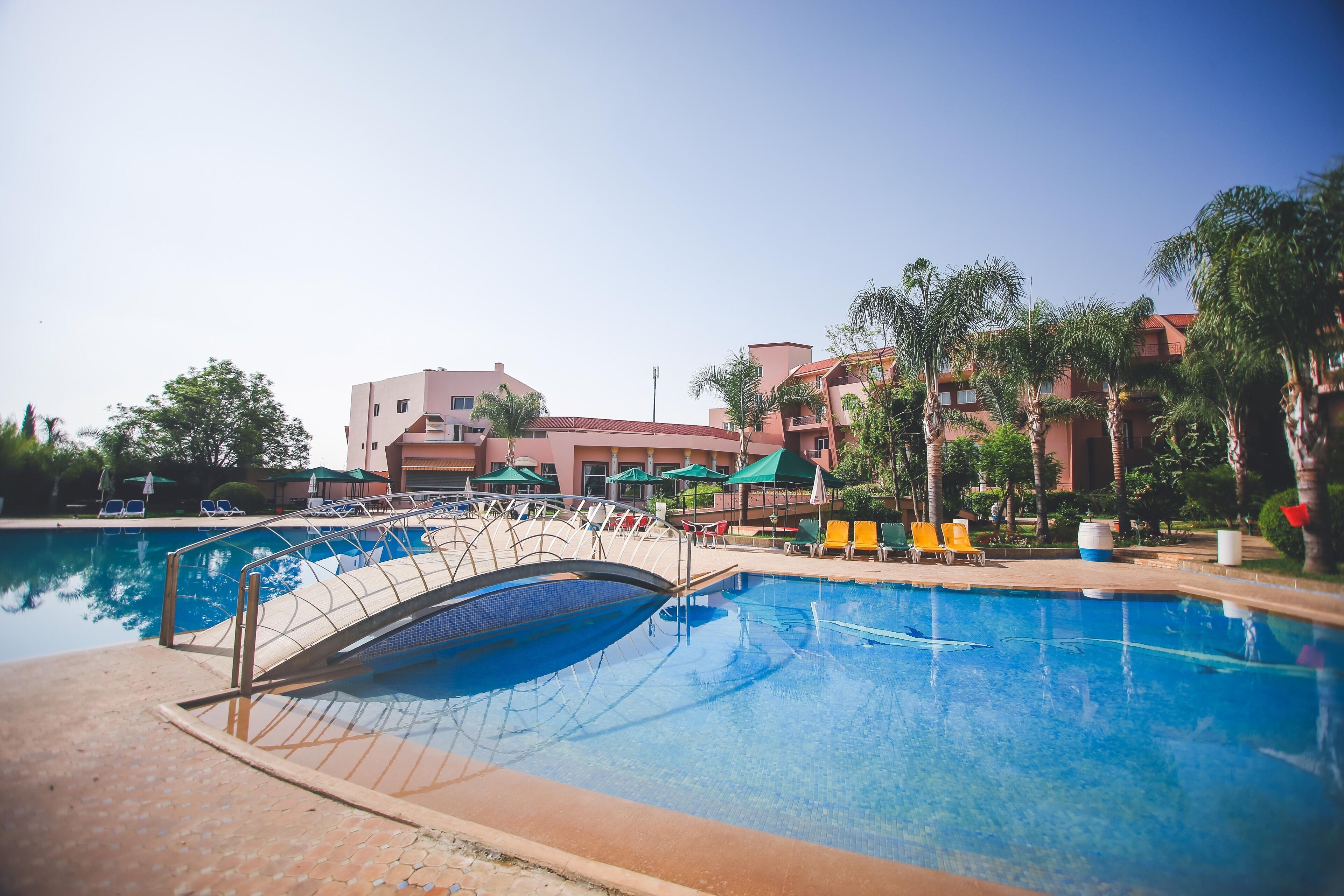 A swimming pool with a bridge, lounge chairs, and palm trees.