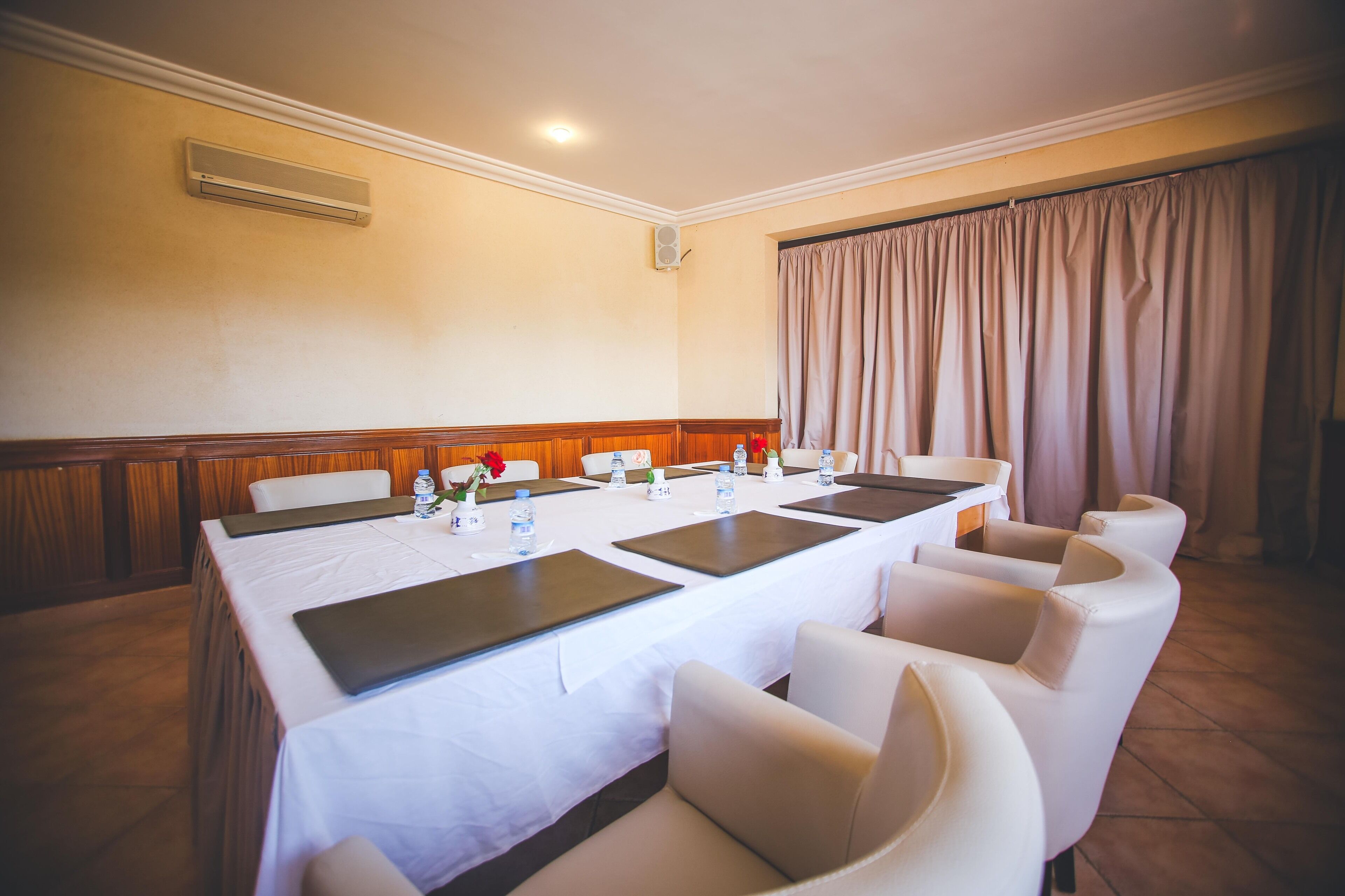 Un salón de conferencias con una mesa larga, sillas blancas y una cortina color crema.