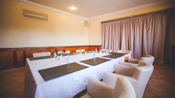 Un salón de conferencias con una mesa larga, sillas blancas y una cortina color crema.
