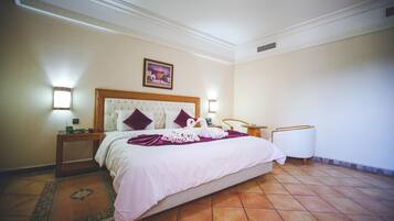 Une chambre d’hôtel avec un grand lit, une table de chevet, une lampe, un tableau accroché au mur et un sol carrelé.