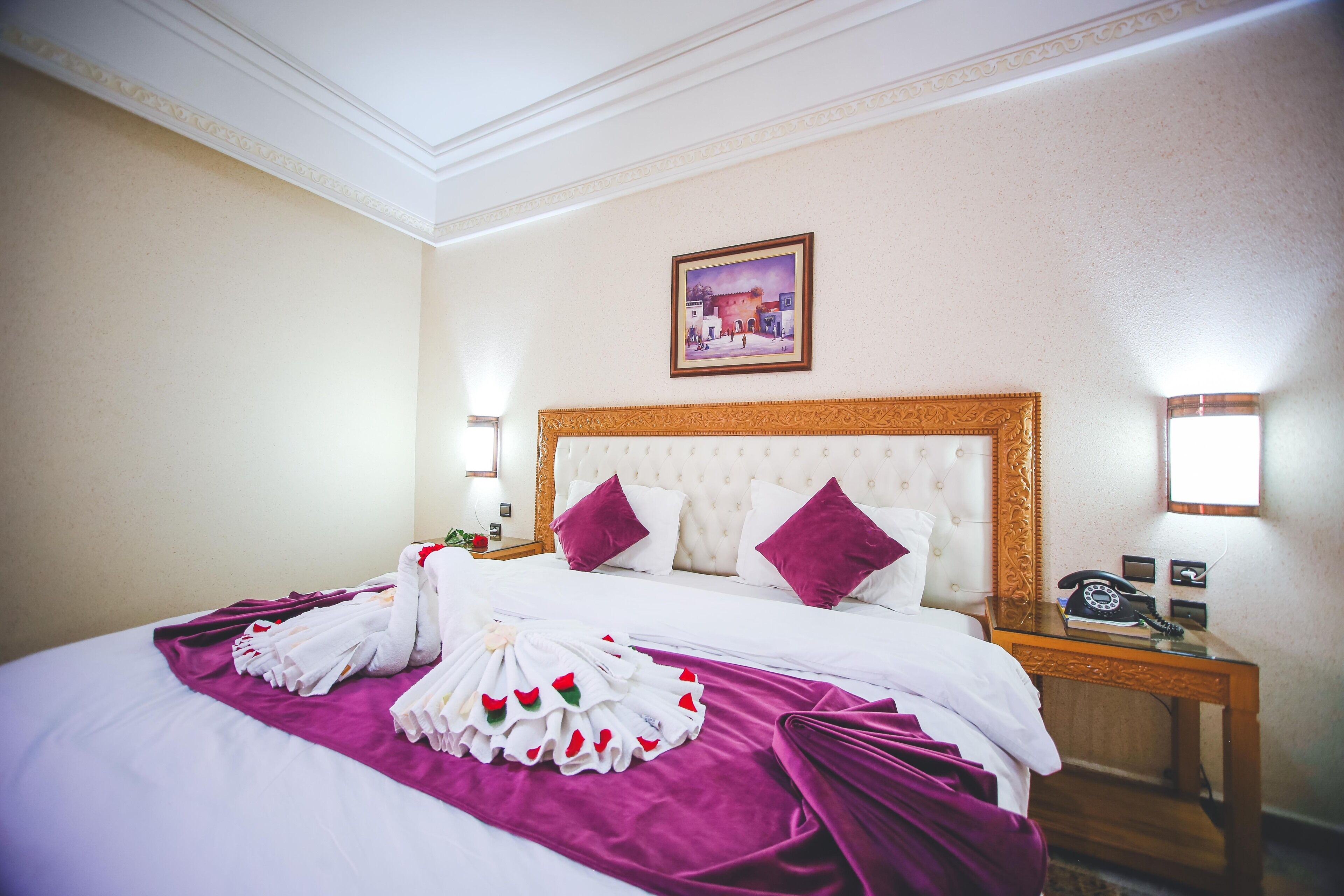 A hotel room with a large bed, a headboard, a nightstand with a telephone, and a painting on the wall.