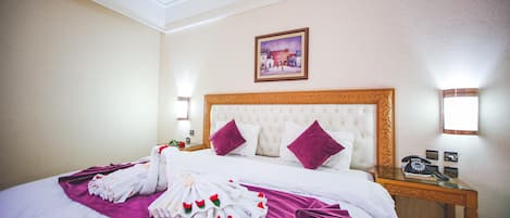 A hotel room with a large bed, a headboard, a nightstand with a telephone, and a painting on the wall.