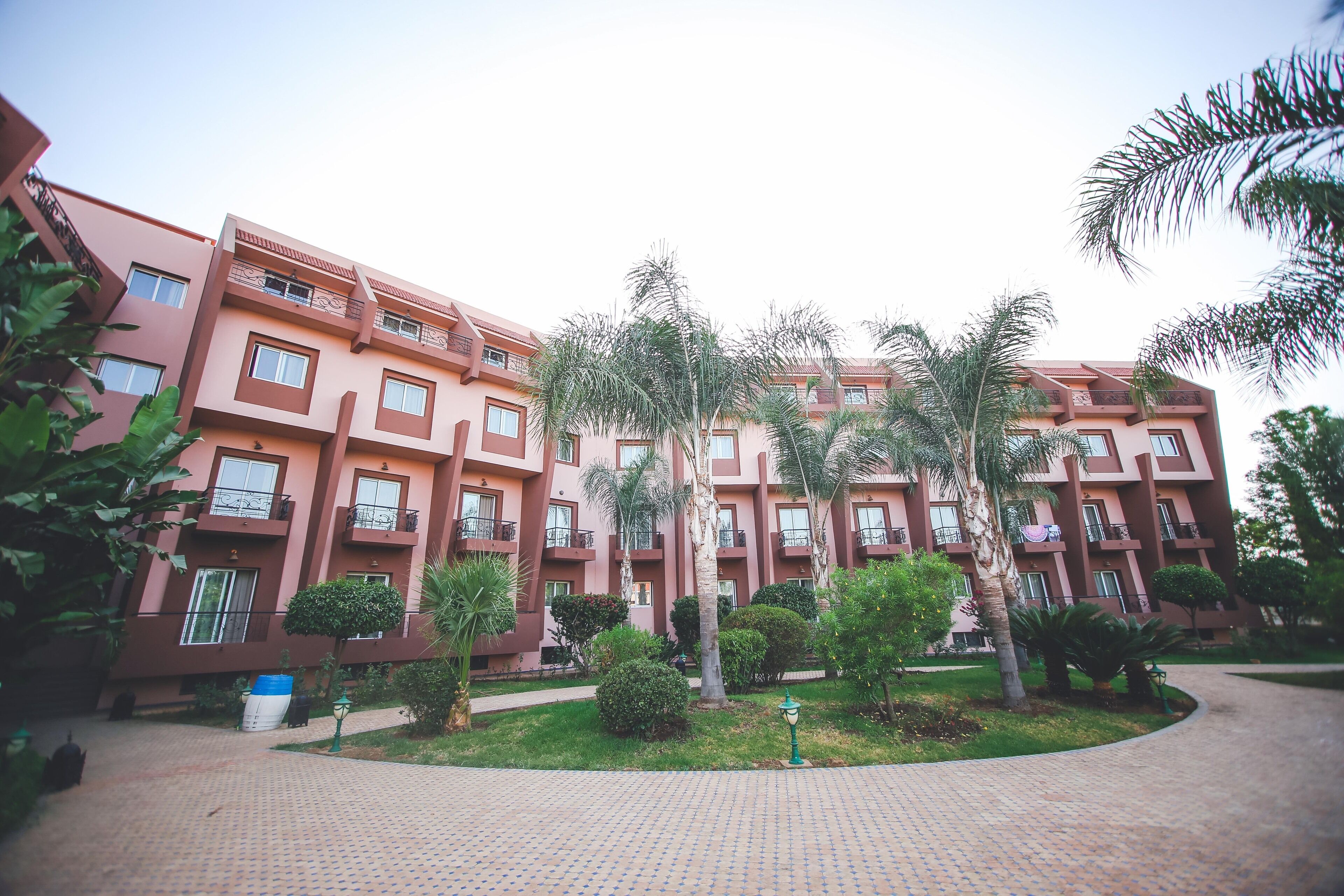 Un edificio de varios pisos con balcones, rodeado de vegetación y un sendero pavimentado.