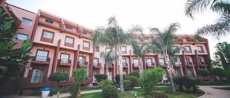 Un edificio de varios pisos con balcones, rodeado de vegetación y un sendero pavimentado.