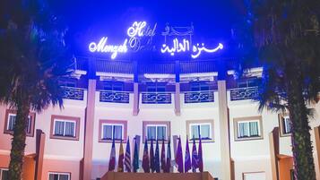 A hotel entrance with a sign in Arabic and English, multiple flags, and a traditional architectural style.