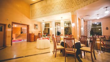 Une salle à manger spacieuse, dotée de hauts plafonds et de motifs décoratifs élaborés sur les murs, avec des chaises et des tables en bois disposées pour le repas.