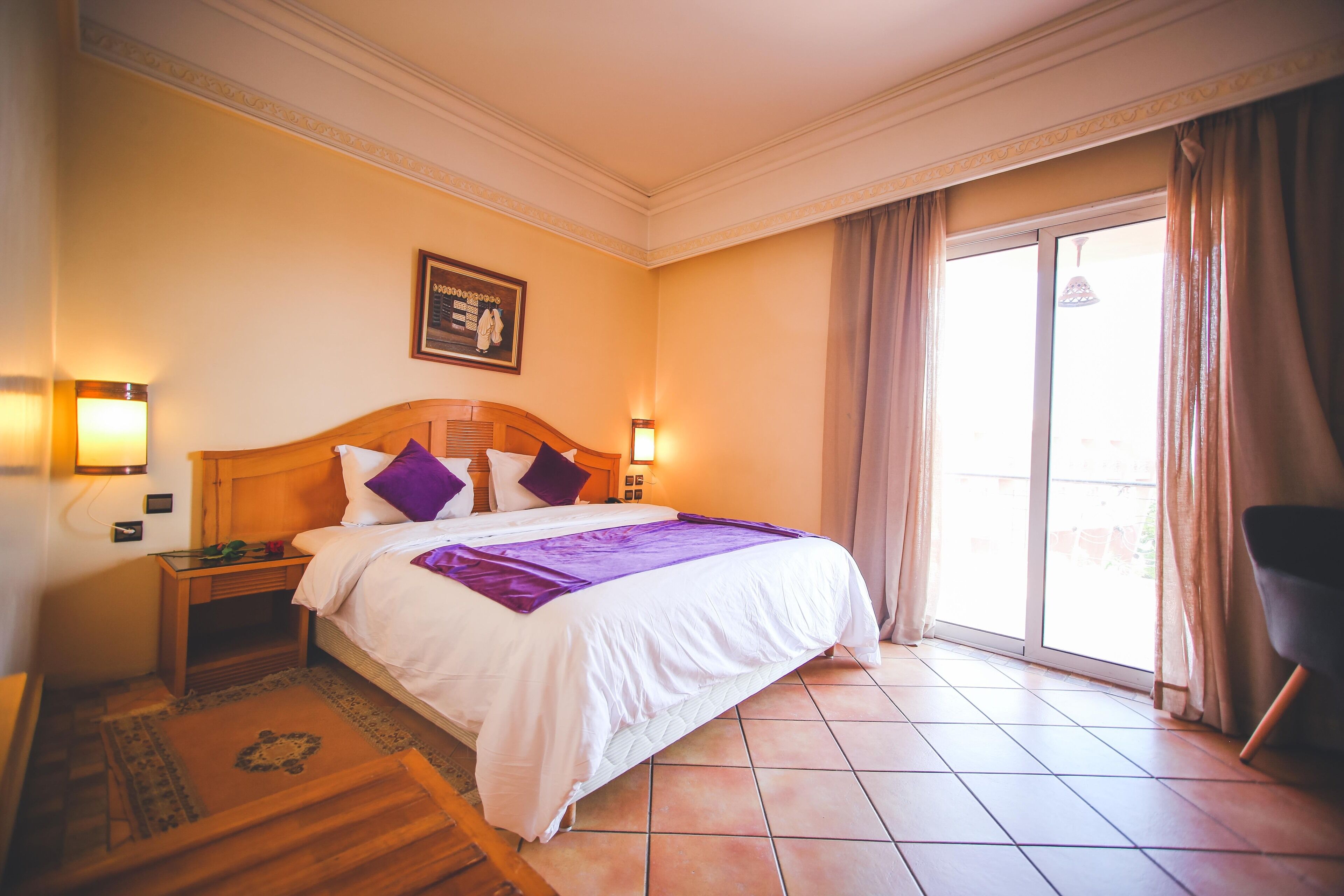 A hotel room with a bed, nightstands, a window with curtains, and a view of the outdoors.