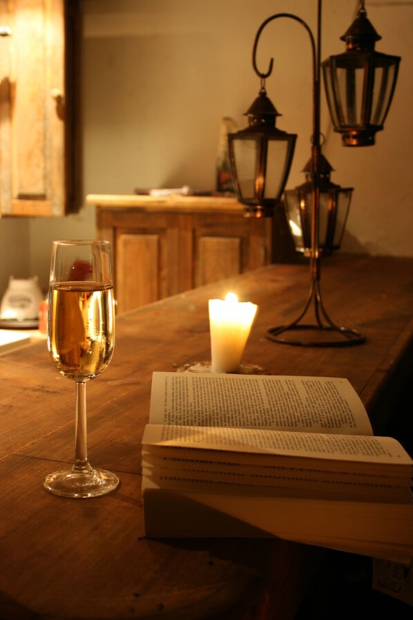 Une table en bois, un verre de vin blanc, une bougie allumée et un livre ouvert.