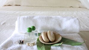 Una cama bien hecha con dosel blanco, una bandeja con toalla, botella y galletas.
