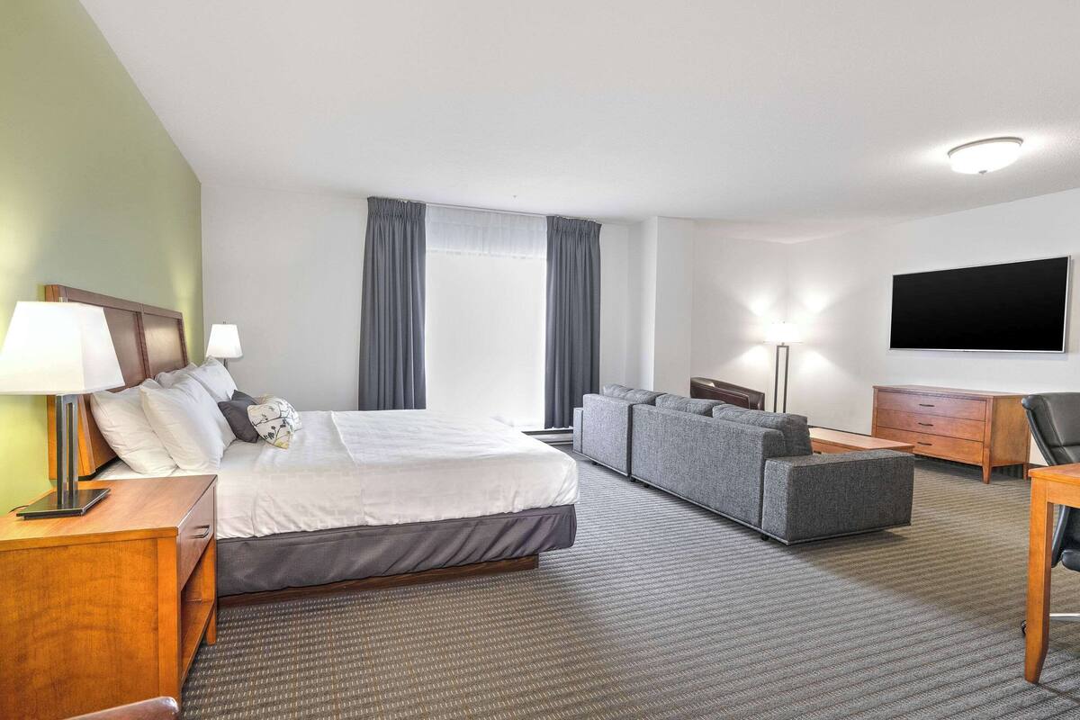 A hotel room with a bed, a sofa, a desk, a TV, and a window with curtains.