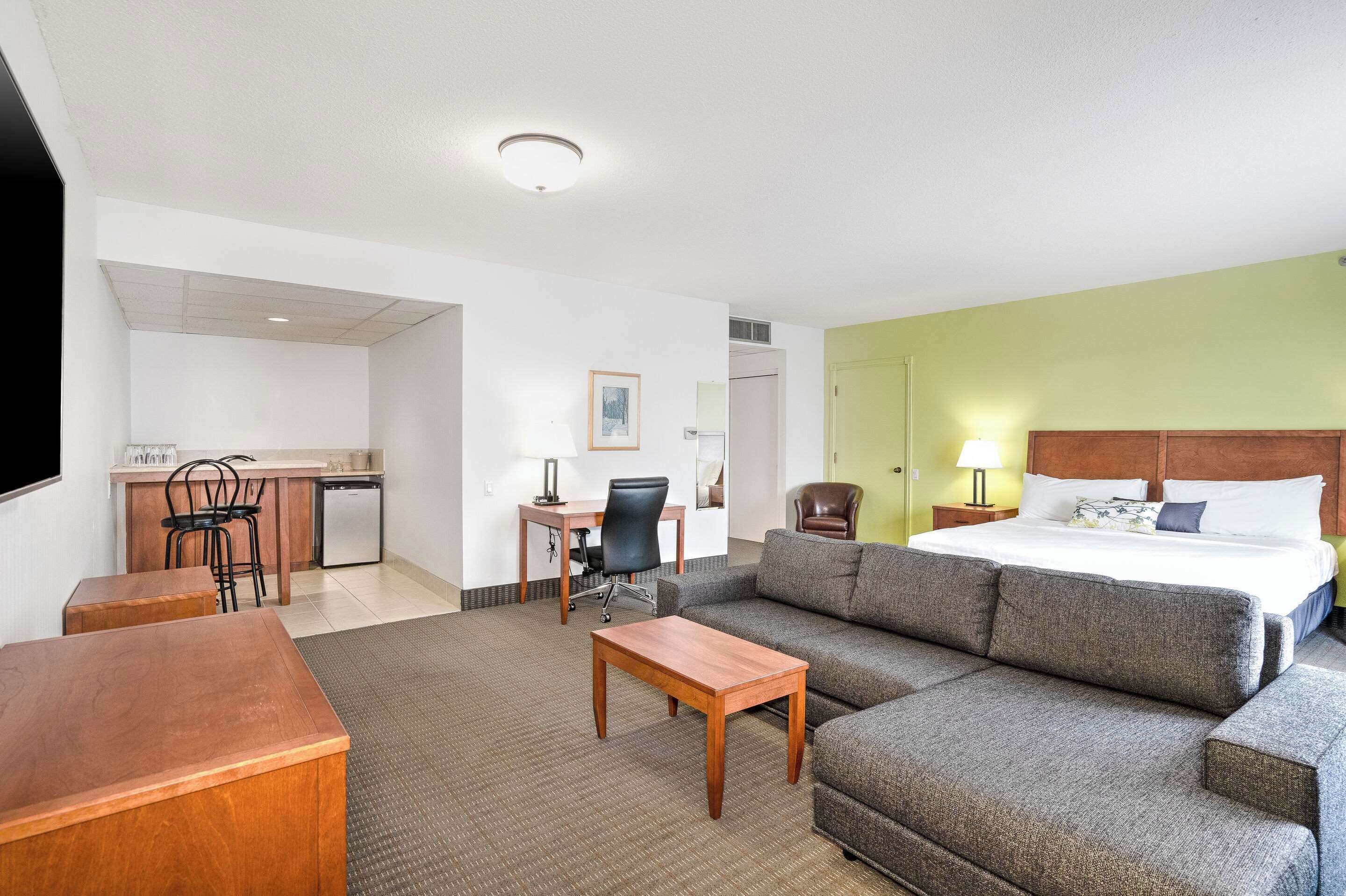 Habitación de hotel con cama, sofá, escritorio con silla, una mesita y una kitchenette.