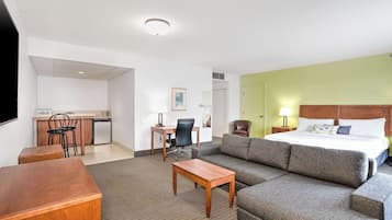 Habitación de hotel con cama, sofá, escritorio con silla, una mesita y una kitchenette.