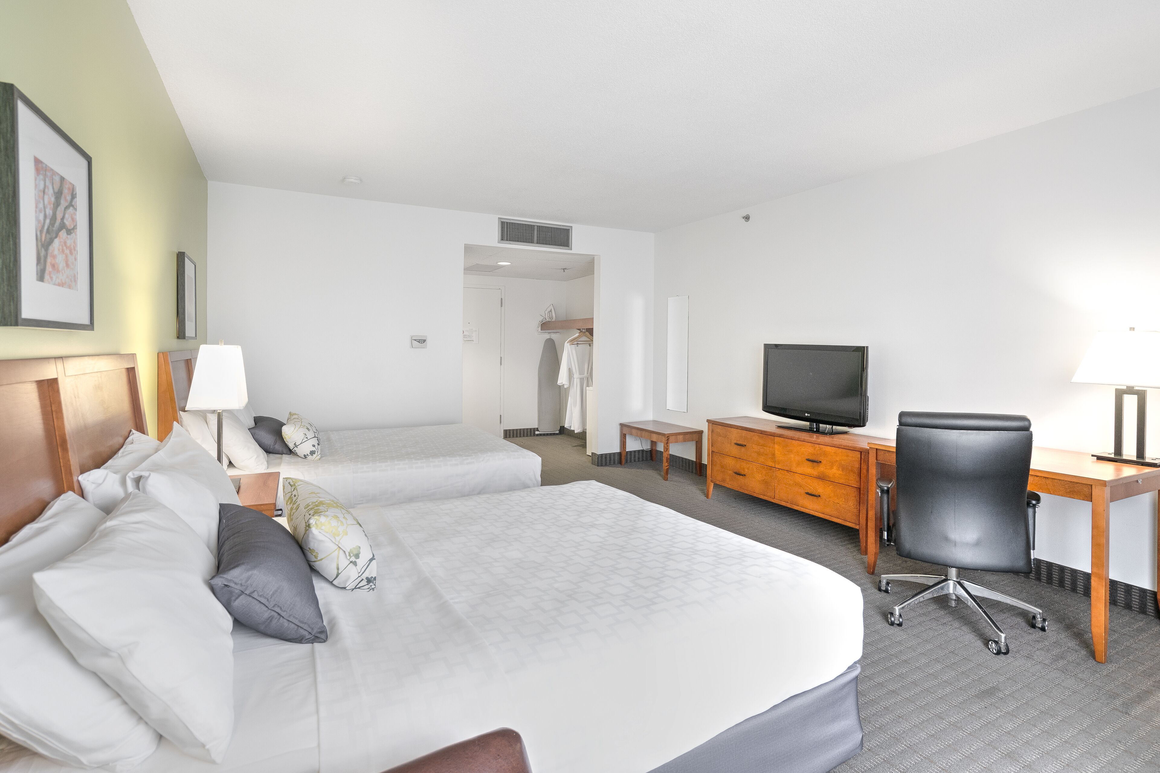 A hotel room with two beds, a desk, a chair, a television, and a wardrobe.