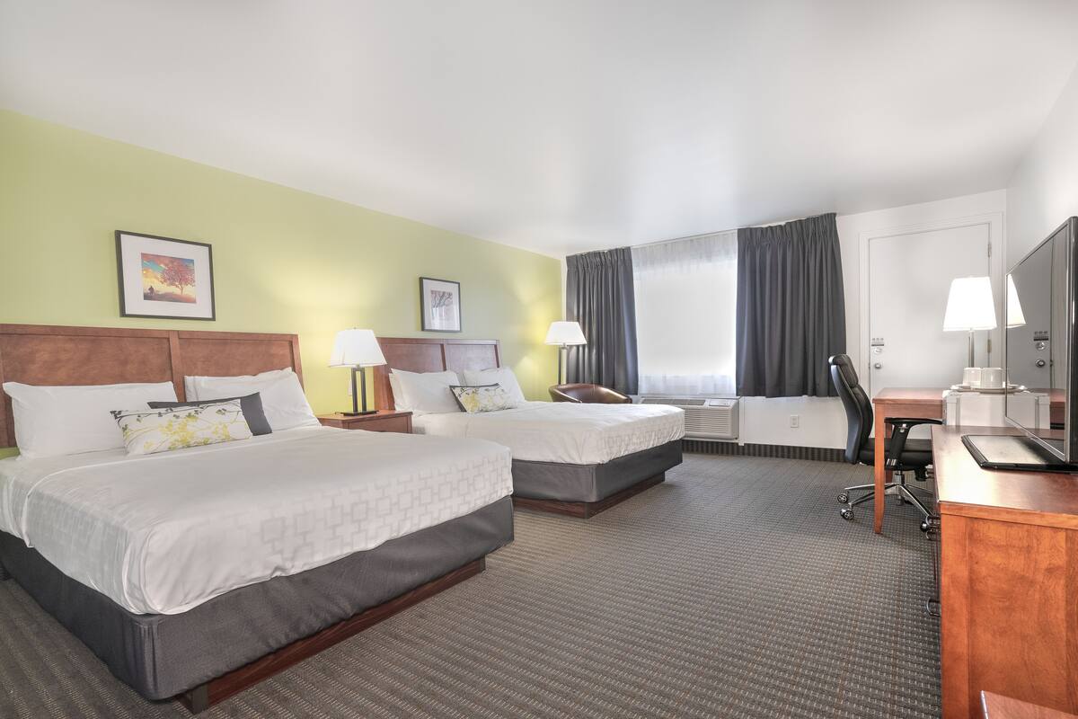 A hotel room with two beds, a desk, a chair, a TV, and a window with curtains.