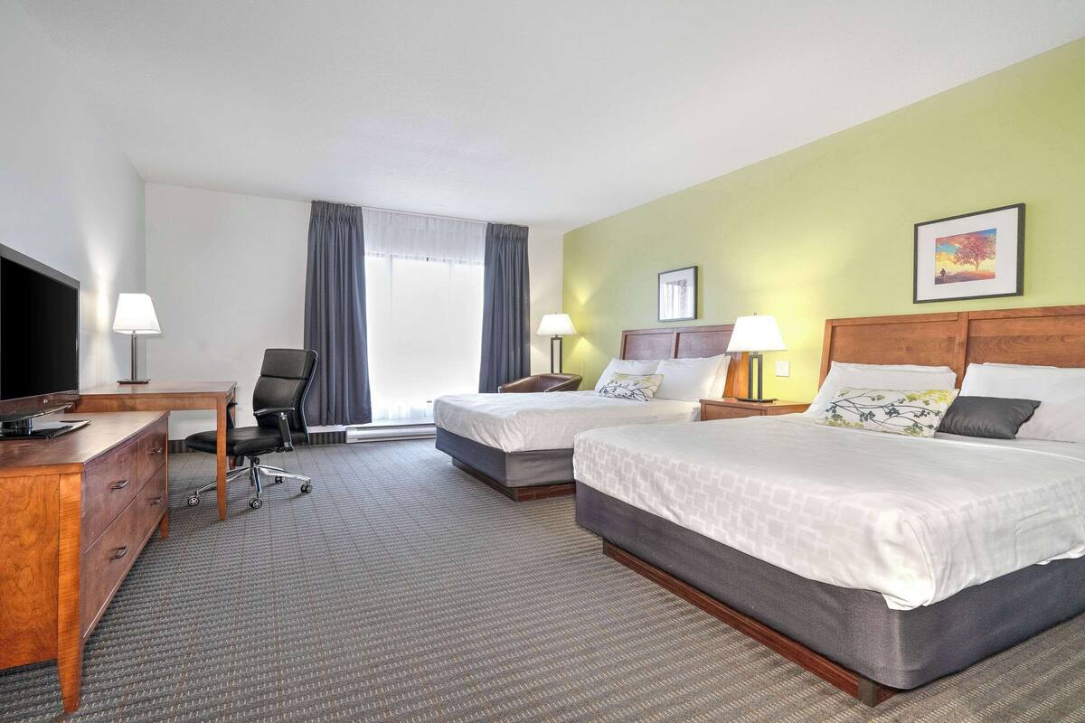 A hotel room with two beds, a desk, a chair, and a TV.