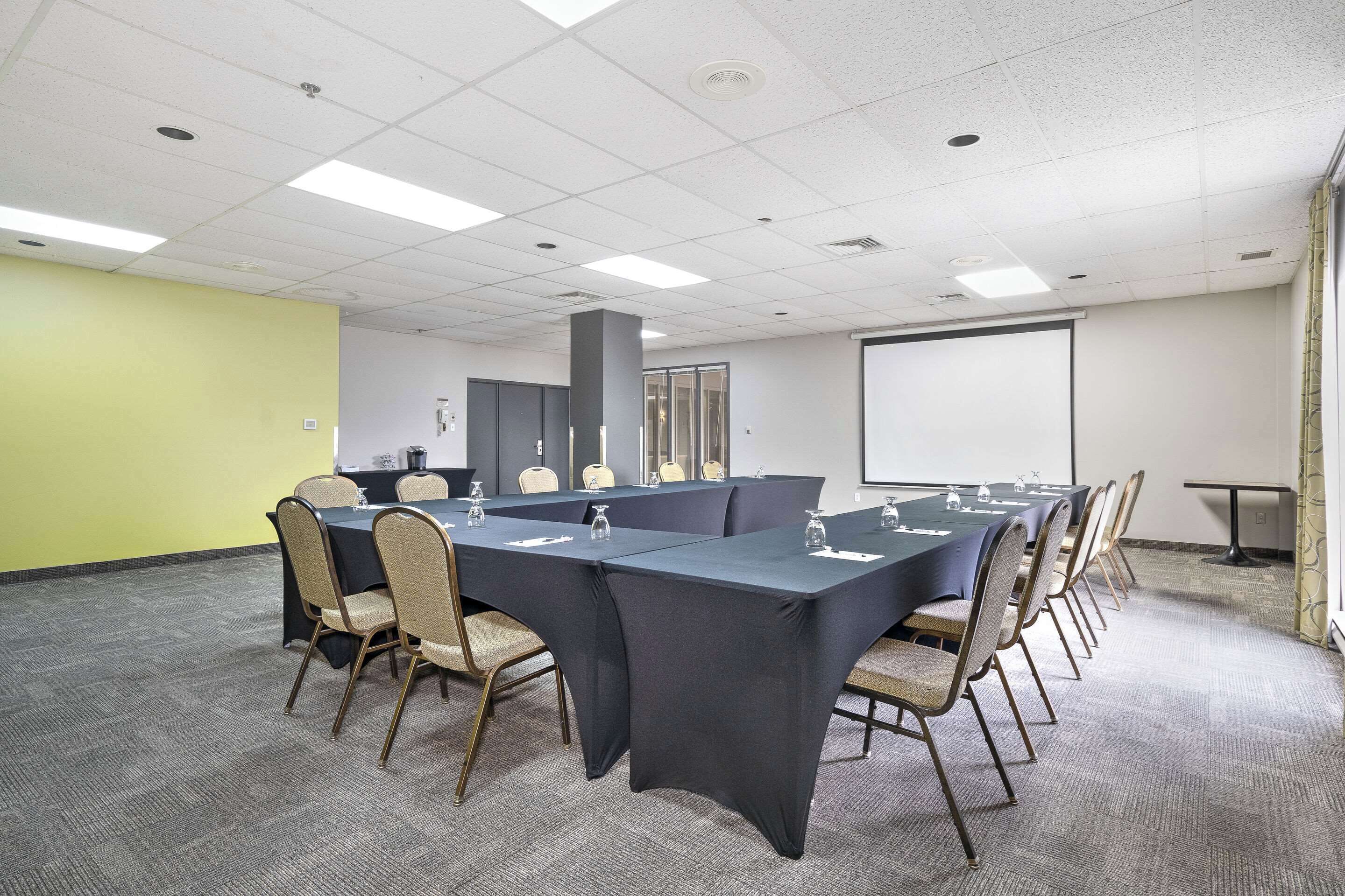 A conference room with a long table, chairs, a projector screen, and a carpeted floor.