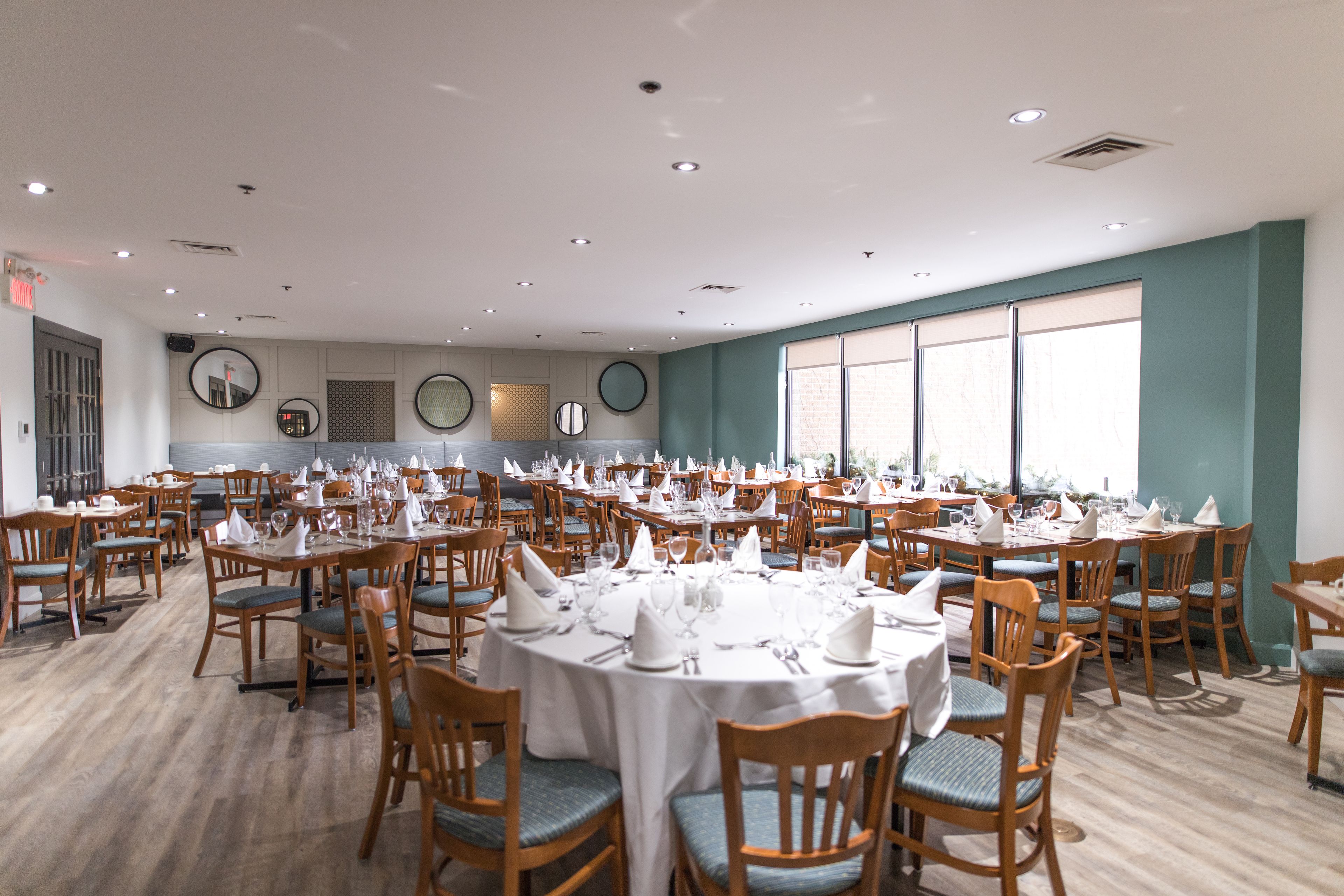 Un amplio comedor con mesas redondas dispuestas para varios invitados, sillas de madera y un diseño moderno en el techo.