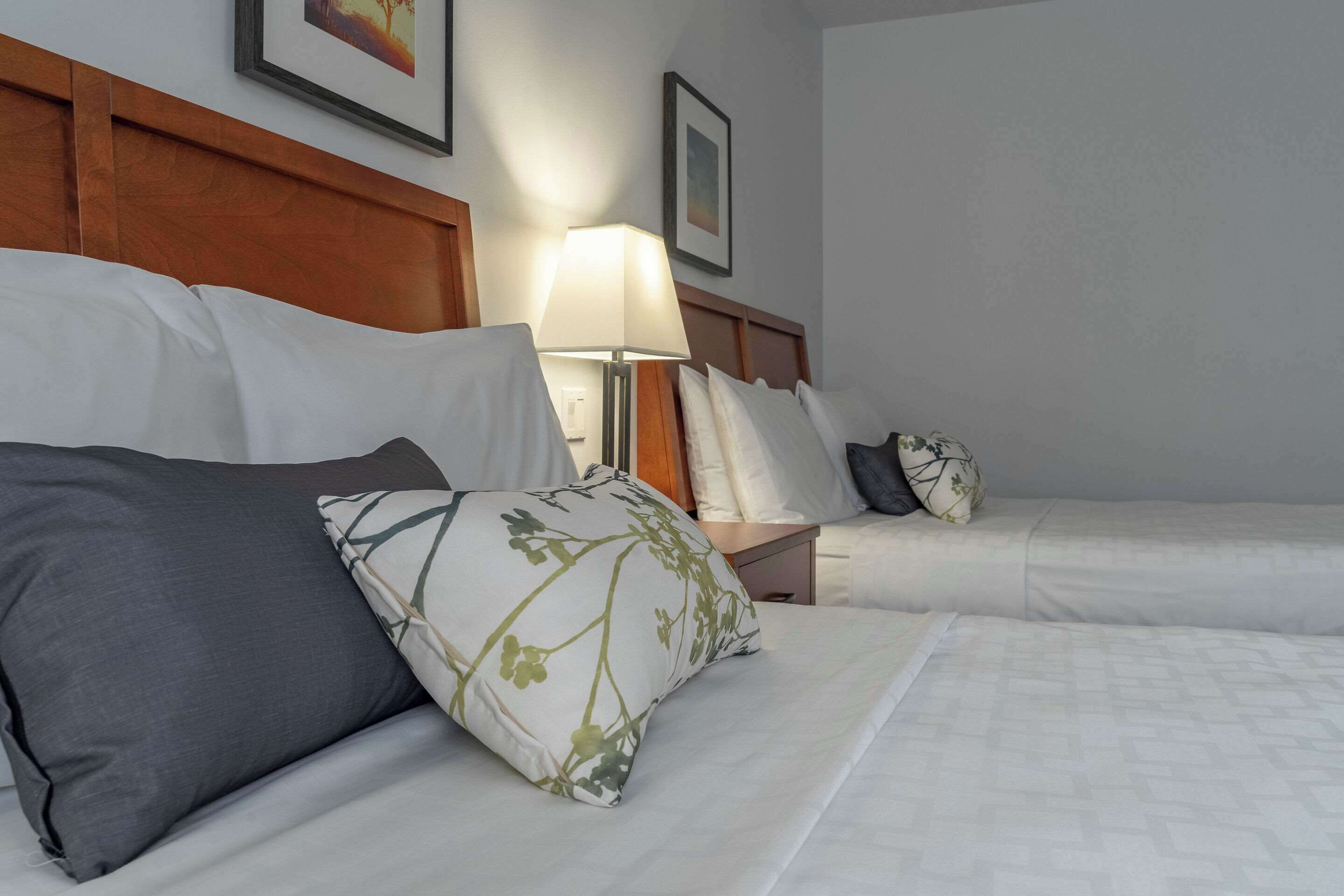 A hotel room with two beds, a nightstand with a lamp, and a framed picture on the wall.