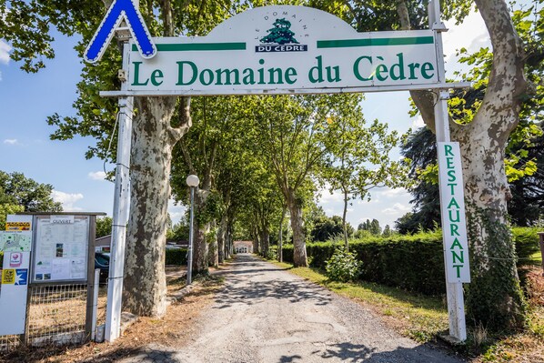 Señalización de Le Domaine du Cedre, un restaurante, con un sendero de tierra que atraviesa una zona arbolada.