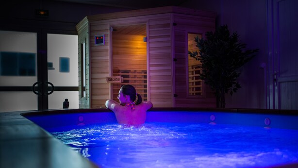 A person relaxing in a heated pool with a sauna sign in the background.