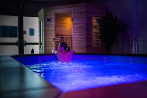 Una persona relajándose en una piscina climatizada, con un cartel de sauna al fondo.