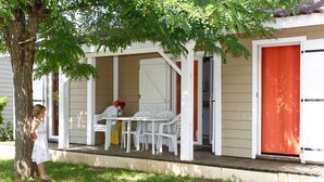 A covered outdoor area with a table and chairs, a tree, and a building with a red door.