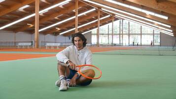 Una cancha de tenis con vigas de madera, una red y un jugador sentado en la cancha.