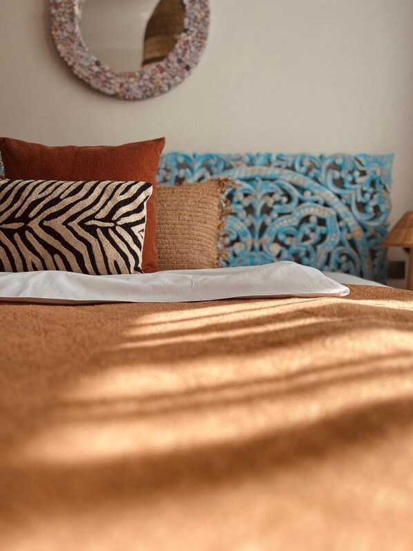 Una cama con sábana blanca, un cojín estampado de cebra, un cojín marrón y un cojín estampado azul.
