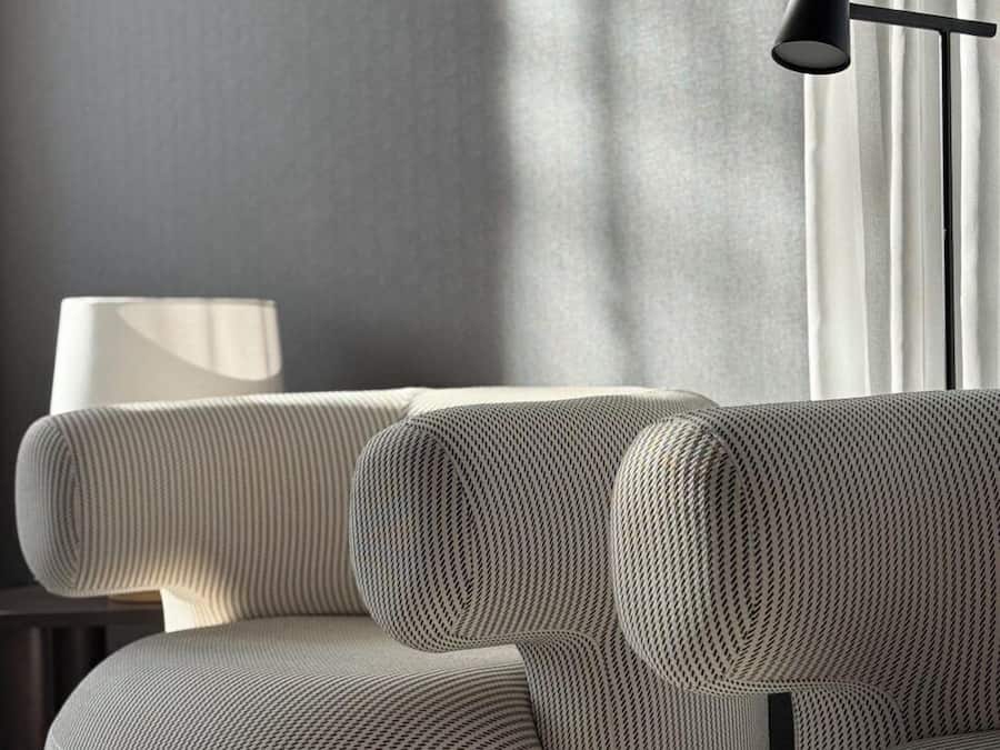 Una sala de estar moderna con un sofá gris, una lámpara de pie y un ventanal con cortinas.