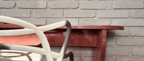 A red metal table with a white chair in front of a brick wall.