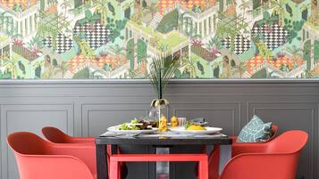 Un coin repas avec un sol à carreaux, une table entourée de chaises rouges et un papier peint aux motifs colorés.