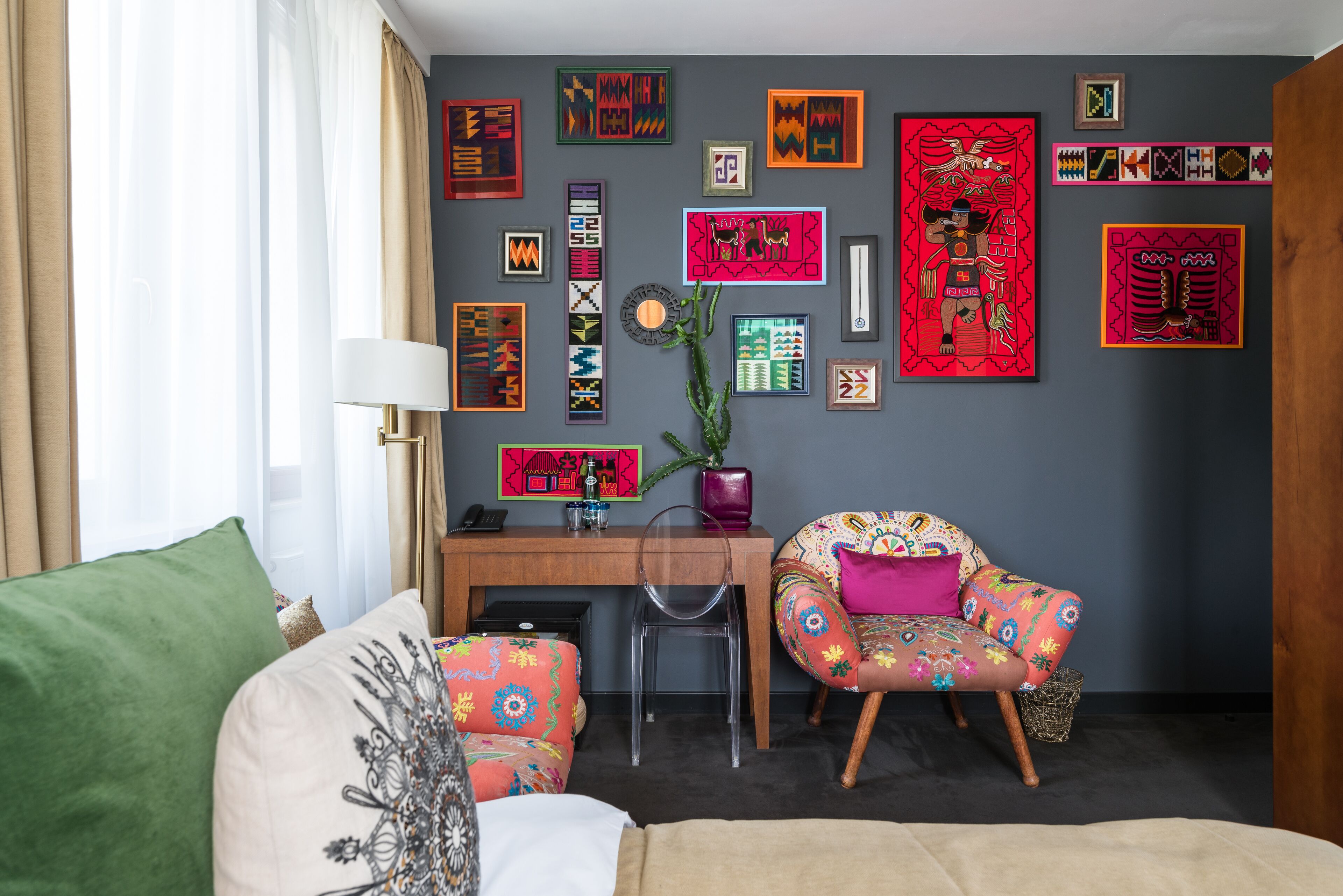 A living room with a desk, two chairs, a couch, and a variety of colorful wall art.
