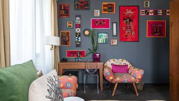 A living room with a desk, two chairs, a couch, and a variety of colorful wall art.