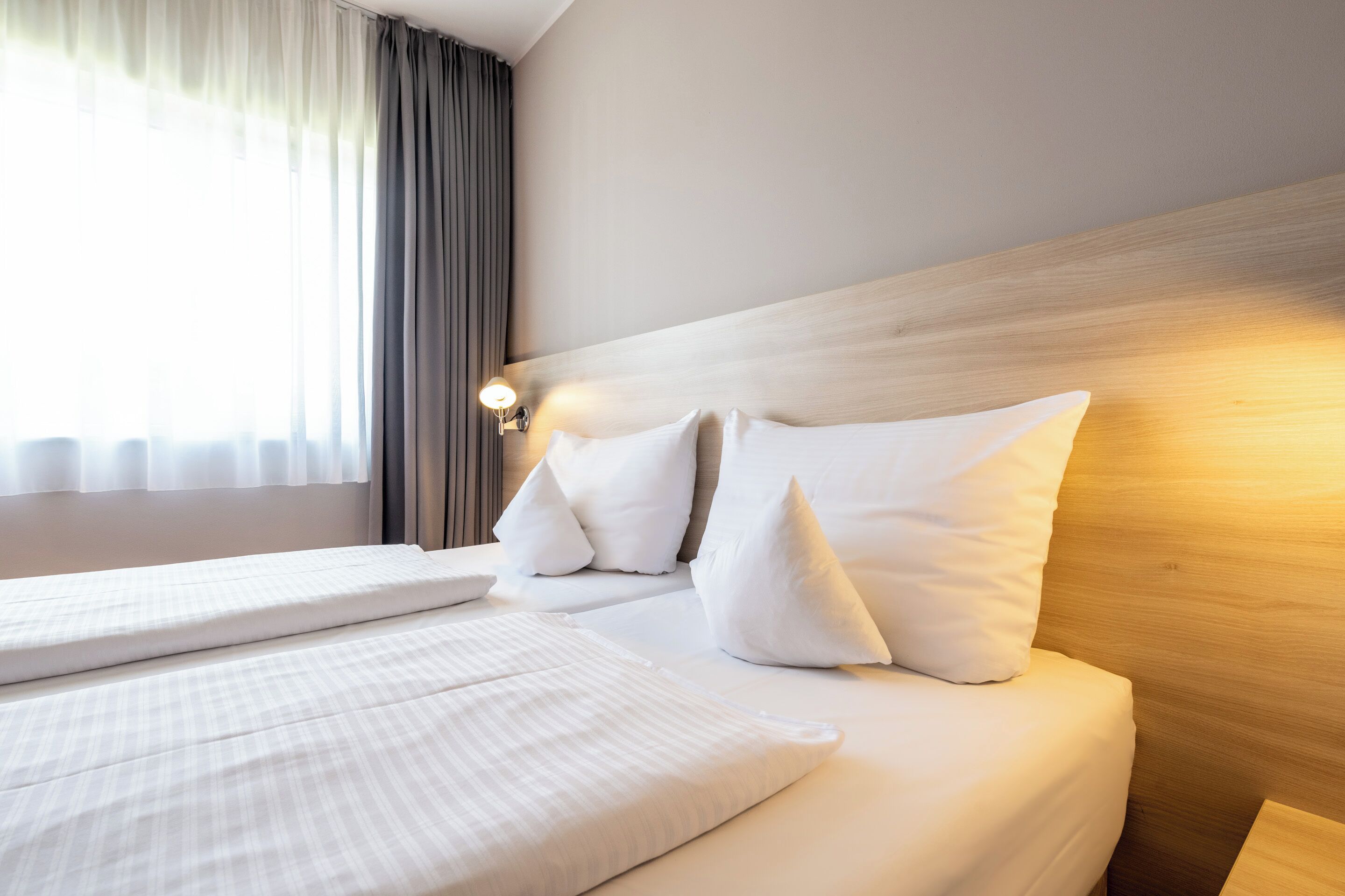 A neatly made bed with white linens and pillows, a wooden headboard, and a bedside lamp.
