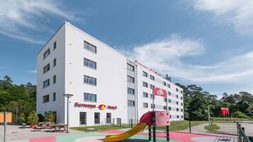 Hotel offers a playground for kids with a slide and climbing structure amidst lush surroundings.