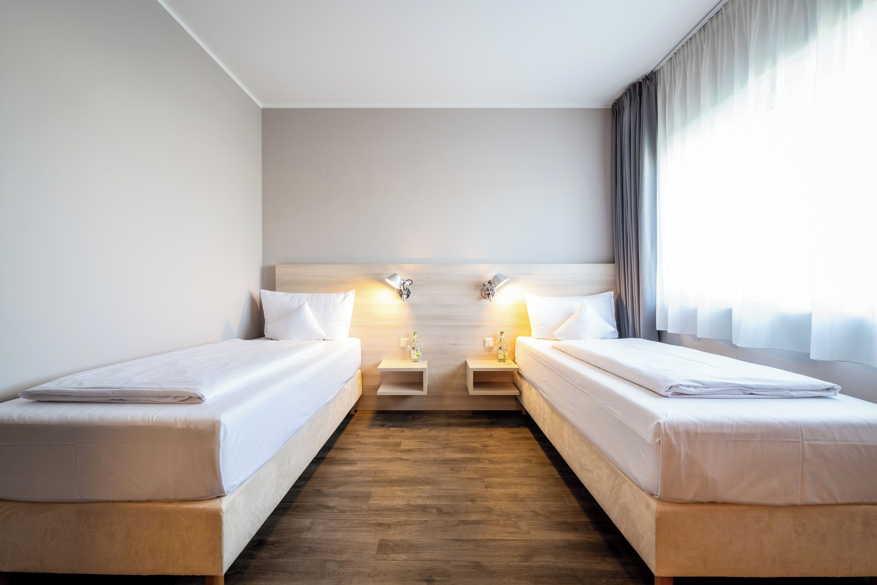 Une chambre d’hôtel avec deux lits, un plancher en bois et une grande fenêtre avec des rideaux.