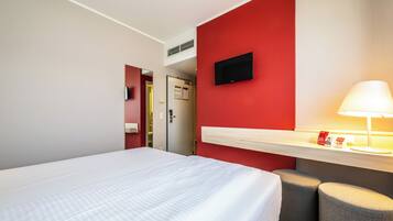 Une chambre d’hôtel avec un lit, un bureau doté d’une lampe et un téléviseur fixé au mur.