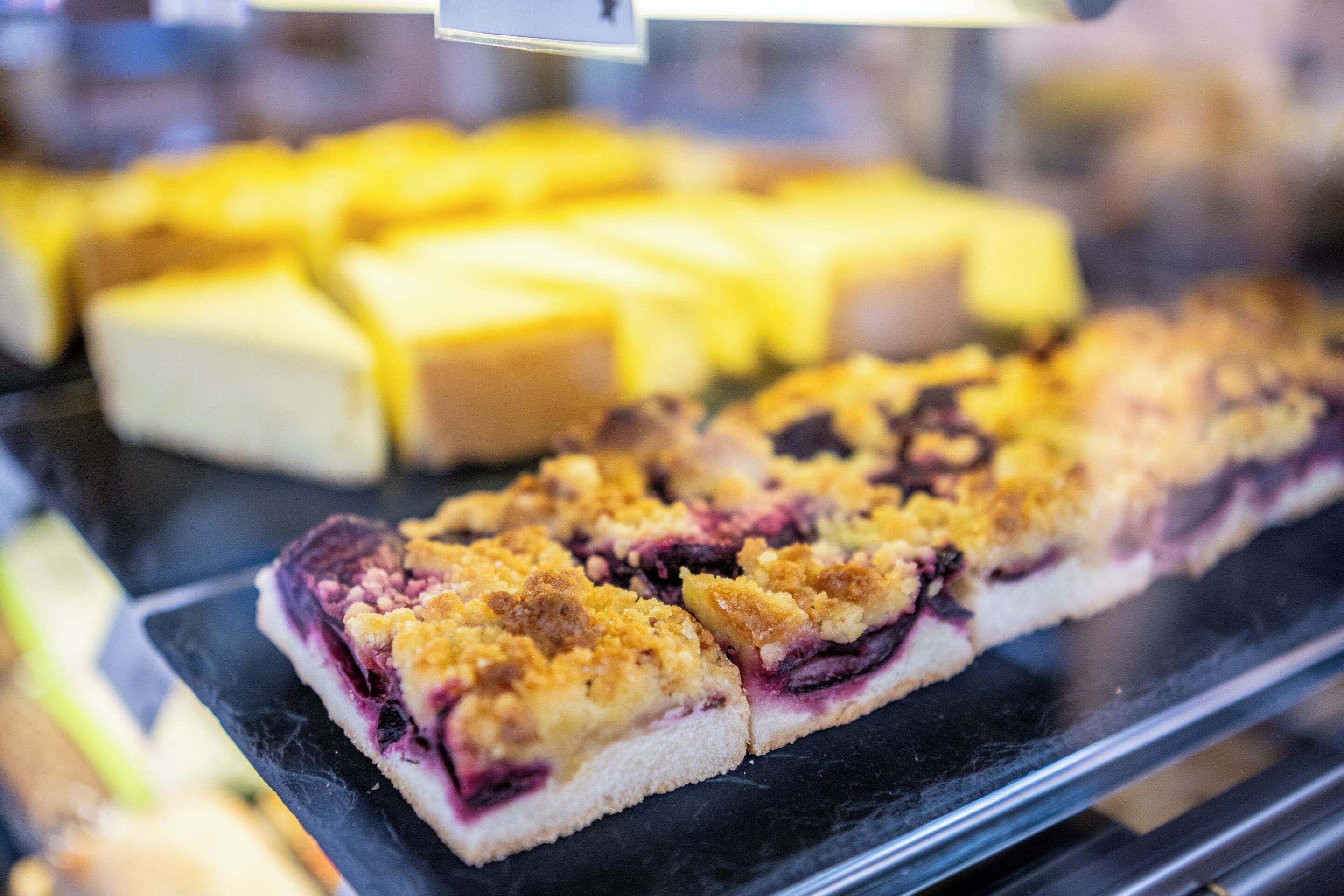 A display of baked goods, including a slice of blueberry crumble pie and several square pastries.