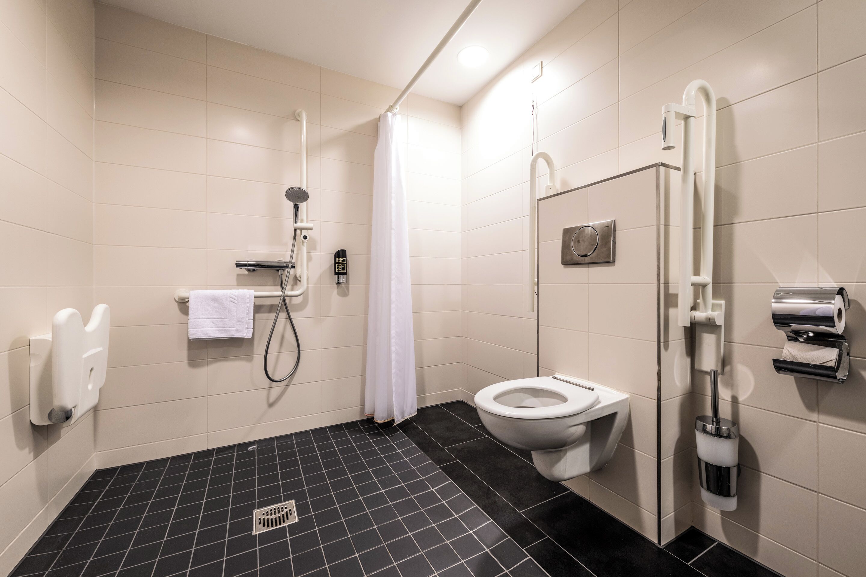 A modern bathroom with a black and white tiled floor, a white toilet, a shower with a handheld showerhead, and a hand dryer.