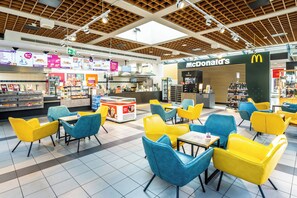 A modern fast-food restaurant with a McDonald's branding, featuring bright yellow and blue seating areas and a variety of food display counters. - Serways Hotel Nürnberg Feucht Ost (Schwarzenbruck)