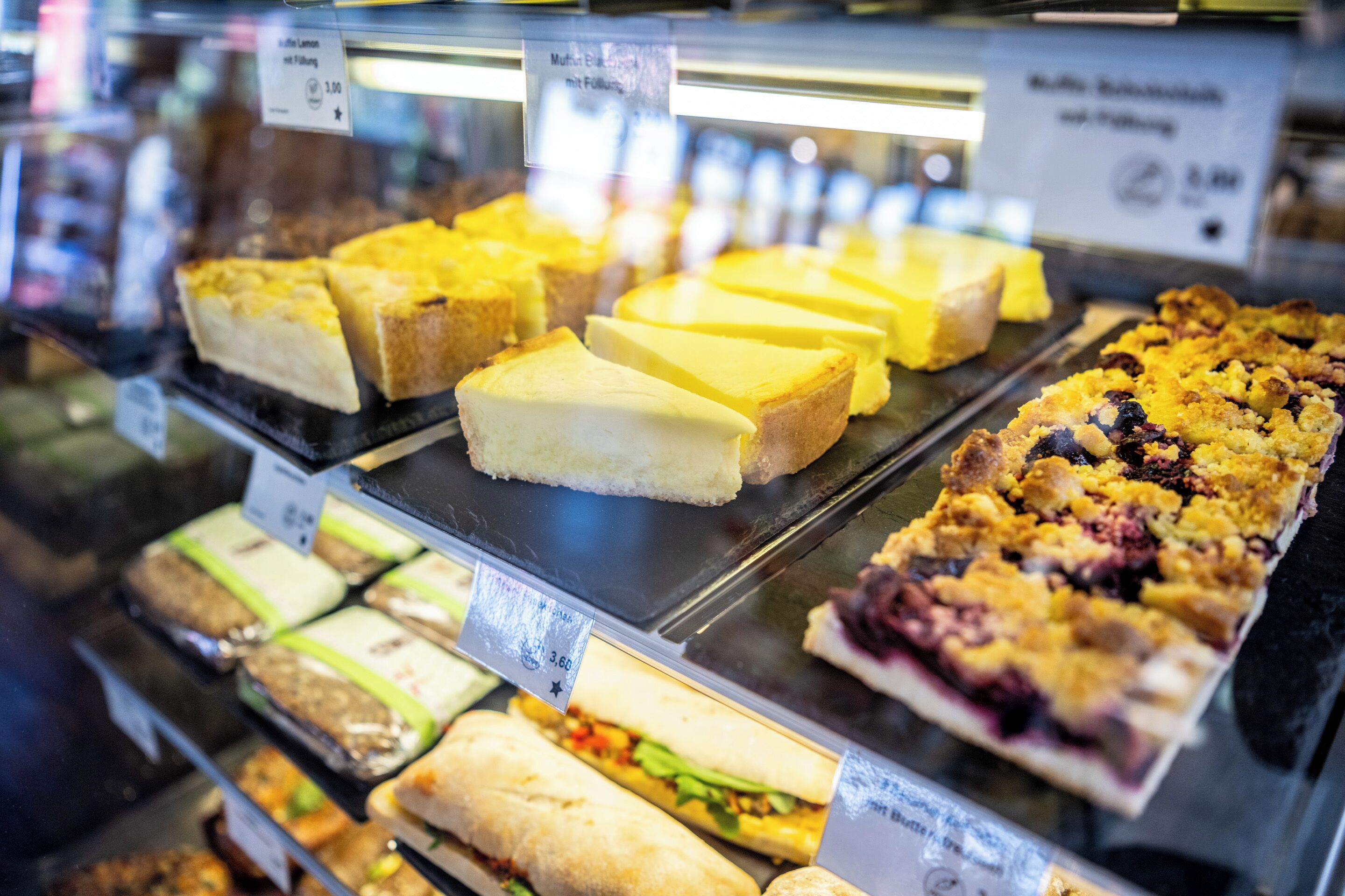 Una vitrina con varios productos de pastelería, incluyendo sándwiches y tartas, con etiquetas de precio visibles.