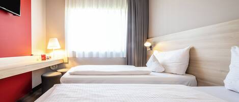 A hotel room with two beds, a desk, a TV, and a window with curtains.