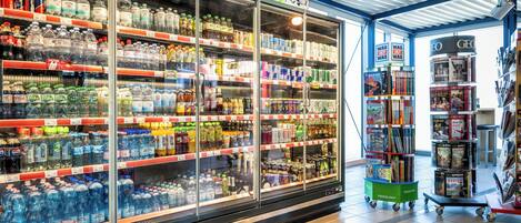 Un supermercado con estantes refrigerados llenos de diversas bebidas, y una sección con libros y revistas.