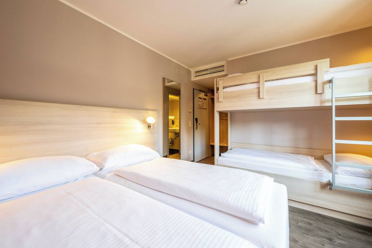 A hotel room with two single beds, a bunk bed, and a mirror.