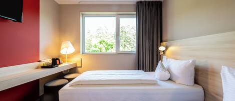 A hotel room with two beds, a desk, a TV, and a window with curtains.