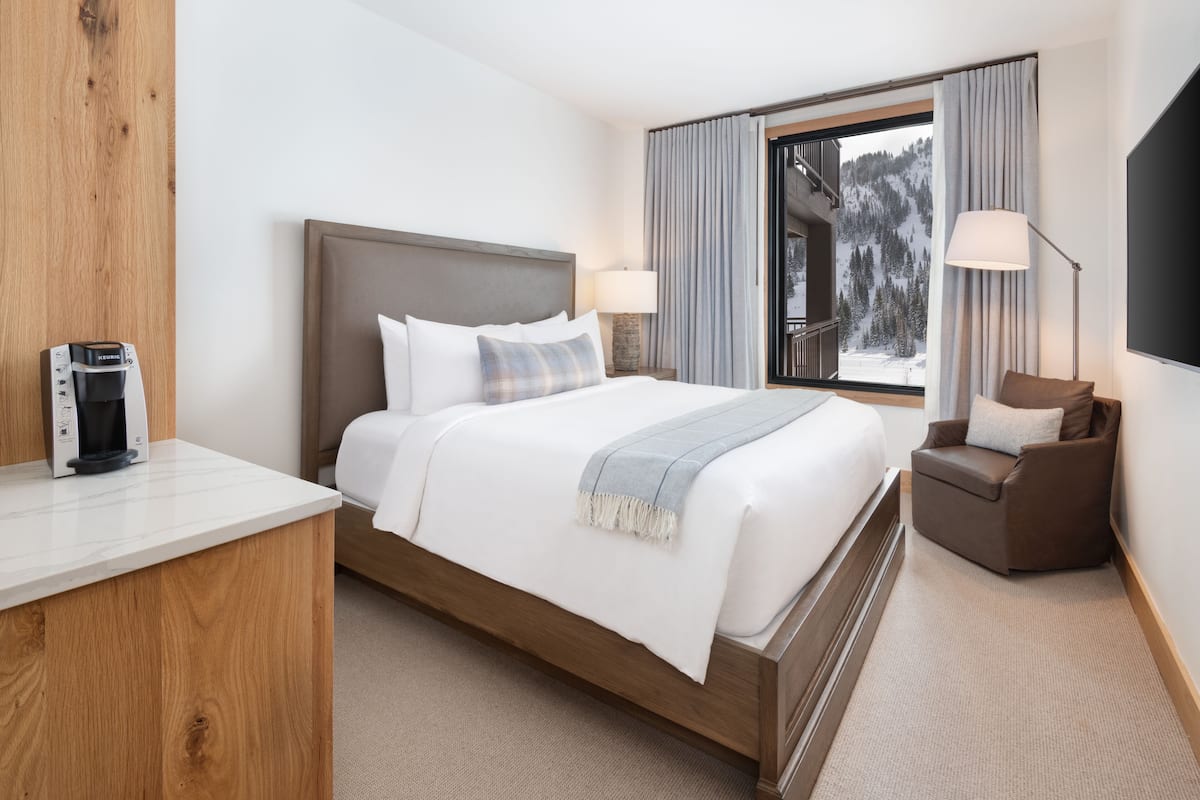 A hotel room with a bed, a chair, a coffee maker, and a window with curtains.