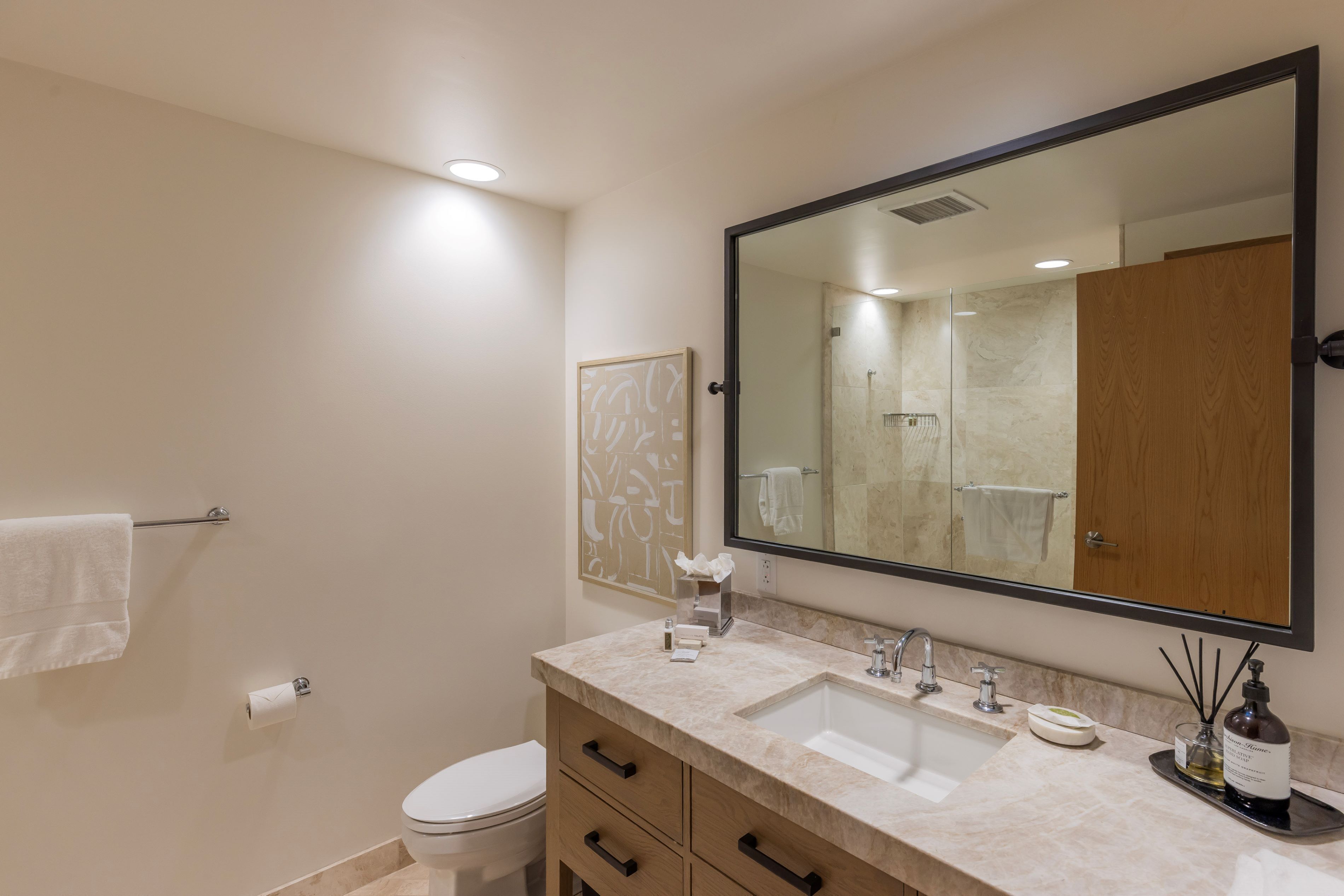 A modern bathroom with a large mirror, two sinks, a toilet, and a towel rack.