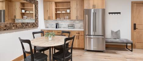 A modern kitchen with wooden cabinets, a stainless steel refrigerator, a round dining table with chairs, and a bench.