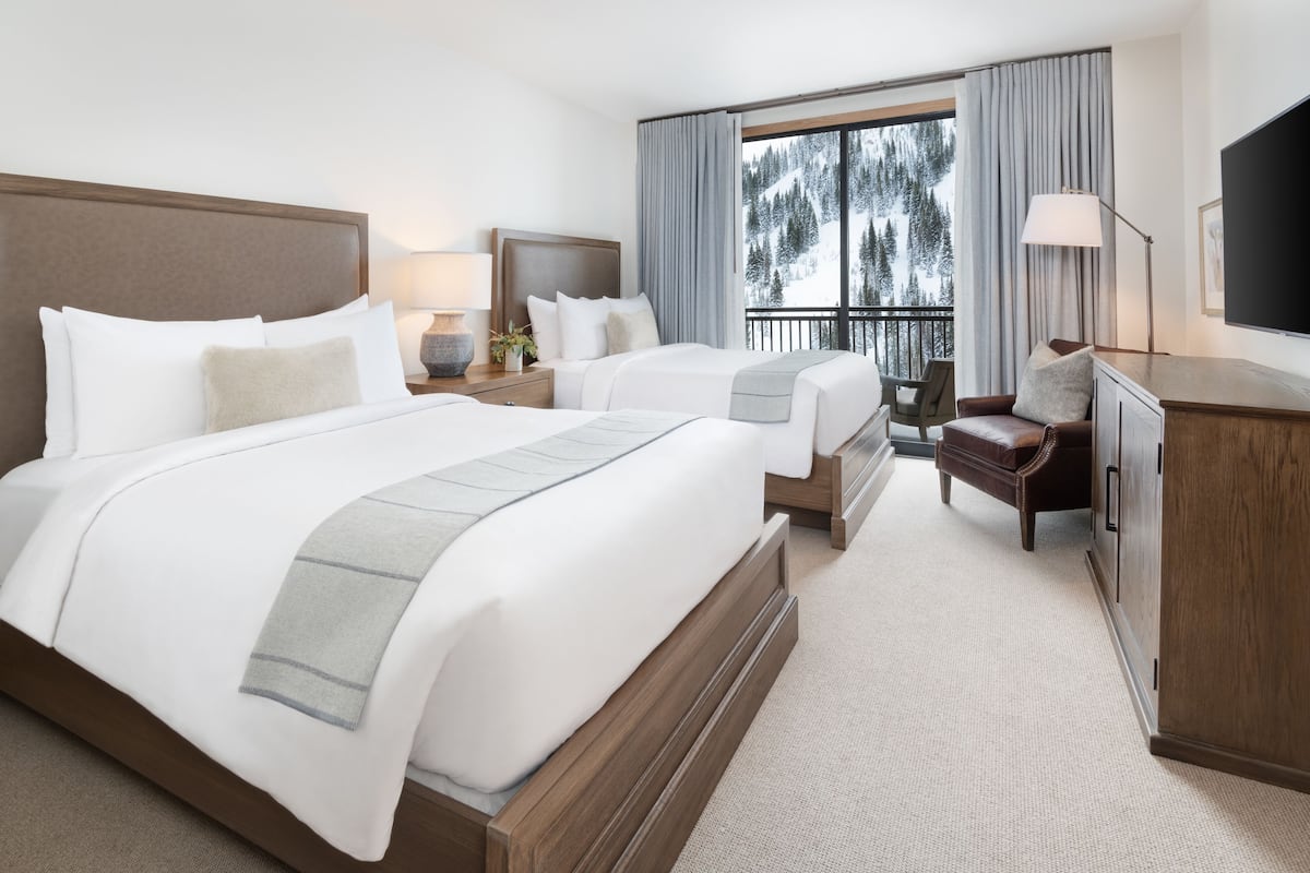 A hotel room with two beds, a desk, a chair, a TV, and a view of a snowy mountain.
